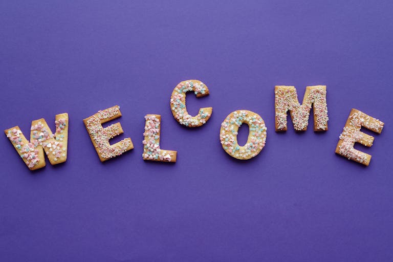 Colorful sprinkled cookies spelling 'welcome' on purple backdrop, perfect for celebrations.